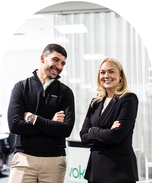 Två Voky-anställda ler med armarna i kors i en kontorsmiljö