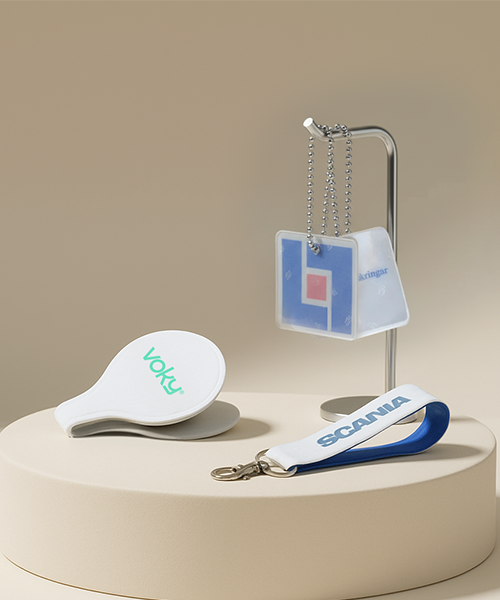 N&auml;rbild av tre reflexprodukter: en vit kl&auml;mreflex (Voky), en h&auml;ngande fyrkantig reflex och en nyckelring (Scania).